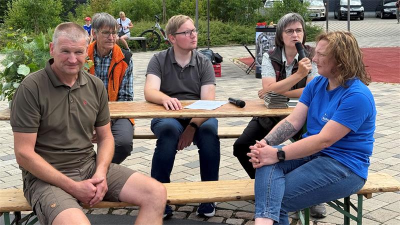 Das Foto zeigt fünf Menschen, die auf Bänken an einem Tisch sitzen.