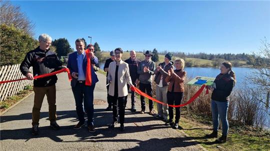 Dr. Alexander Saipa und Carola Schmidt schneiden am Buntenbocker Sumpfteich das rote Band durch und öffnen den Klimalehrpfad offiziell. Mit dabei sind weitere Projektpartner wie die Landesforsten.