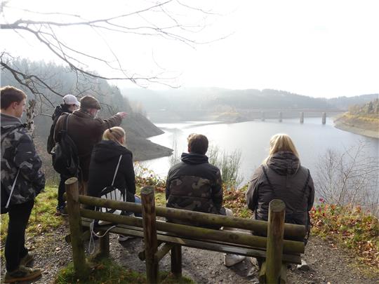 Dr. Rainer Bendick (3. v. li.) zeigt der Gruppe, wo das Gräberfeld und das Barackenlager waren. Das Lager lag unterhalb der heutigen Weißwasserbrücke. Fotos: Römhild; Grafik: OpenStreetMap/Exner