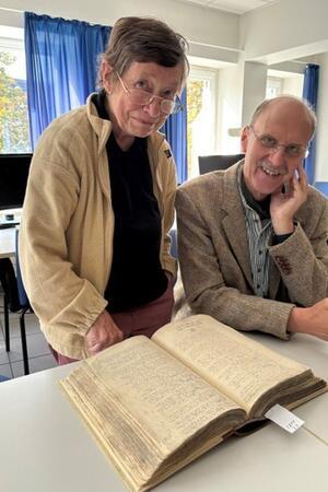 Hopfenspeicher soll zum Ort für Geschichte und Kultur werden Zwei ältere Personen betrachten ein aufgeschlagenes, altes Buch auf einem Tisch in einem hellen Raum mit blauen Vorhängen