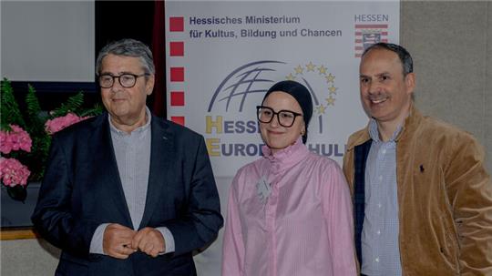 Drei Personen stehen vor einem Banner mit dem Schriftzug 'Hessisches Ministerium für Kultus, Bildung und Chancen' und 'HESSEN EUROPA SCHULE'