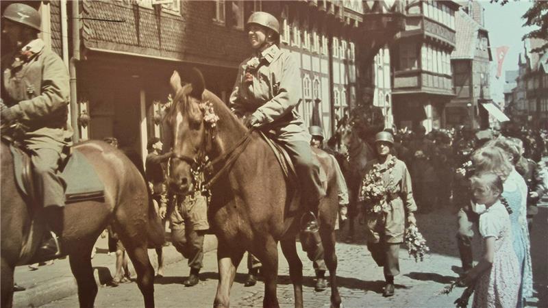 Reiter in Uniform mit Helm auf Pferd in einer belebten historischen Stadtstraße mit Passanten