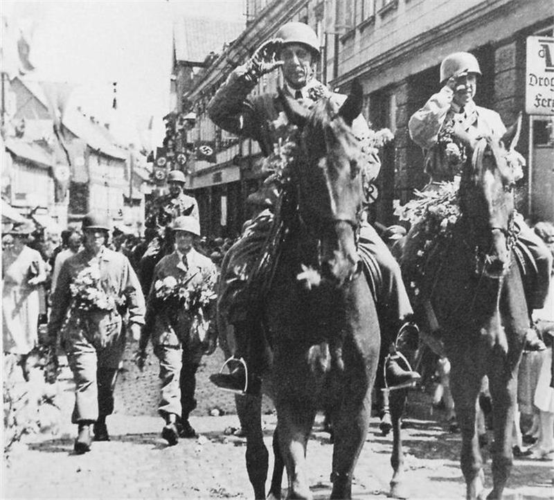 Soldaten in Uniformen reiten auf Pferden und marschieren durch eine mit Fahnen geschmückte Straße