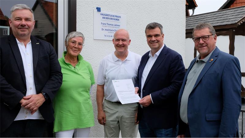 Mehrere Menschen stehen nebeneinander, vier Männer und eine Frau. Einer hält eine Urkunde in der Hand.