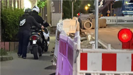 Das Foto zeigt zwei Mopedfahrer, die ihr Moped über den Gehweg schieben.
