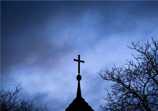 Dunkle Wolken über einem Kreuz einer Kirche: Einem der Opfer muss dSchadenersatz gezahlt werden (Symbolbild).