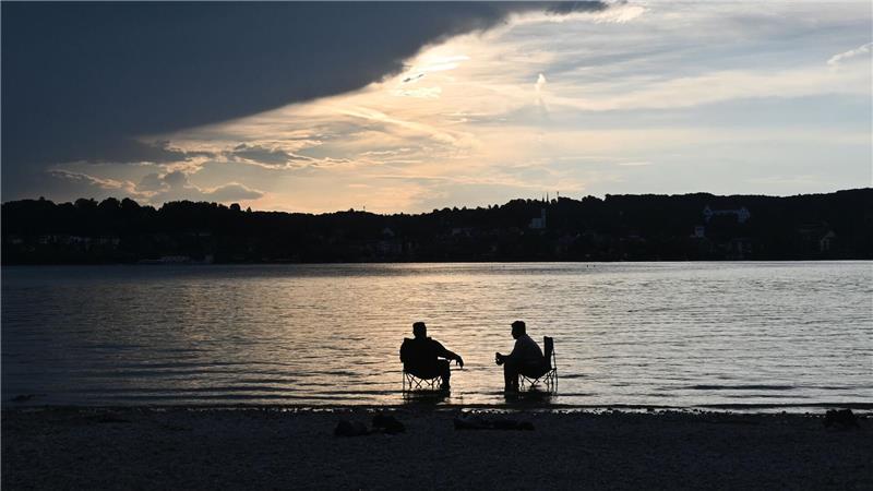 Bilder des Tages Dunkle Wolken ziehen über den Starnberger See während zwei Männer mit Campingstühlen im Wasser sitzen.