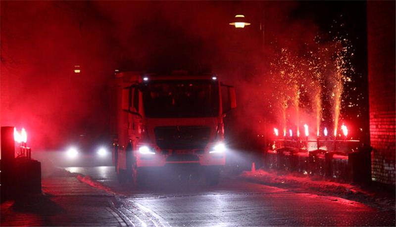 Ein Feuerwehrfahrzeug rollt über eine Brücke, links und rechts davon brennen bengalische Lichter.