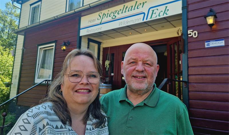 Zwei lächelnde Personen stehen vor einem Gebäude mit dem Schild 'Spiegeltaler Eck'.