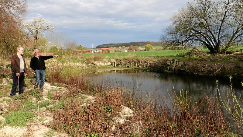 Zwei Personen blicken auf einen fast leeren Teich, an dessen Ufern Schlammreste liegen.