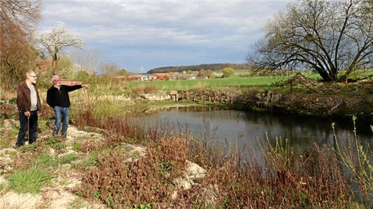Zwei Personen blicken auf einen fast leeren Teich, an dessen Ufern Schlammreste liegen.