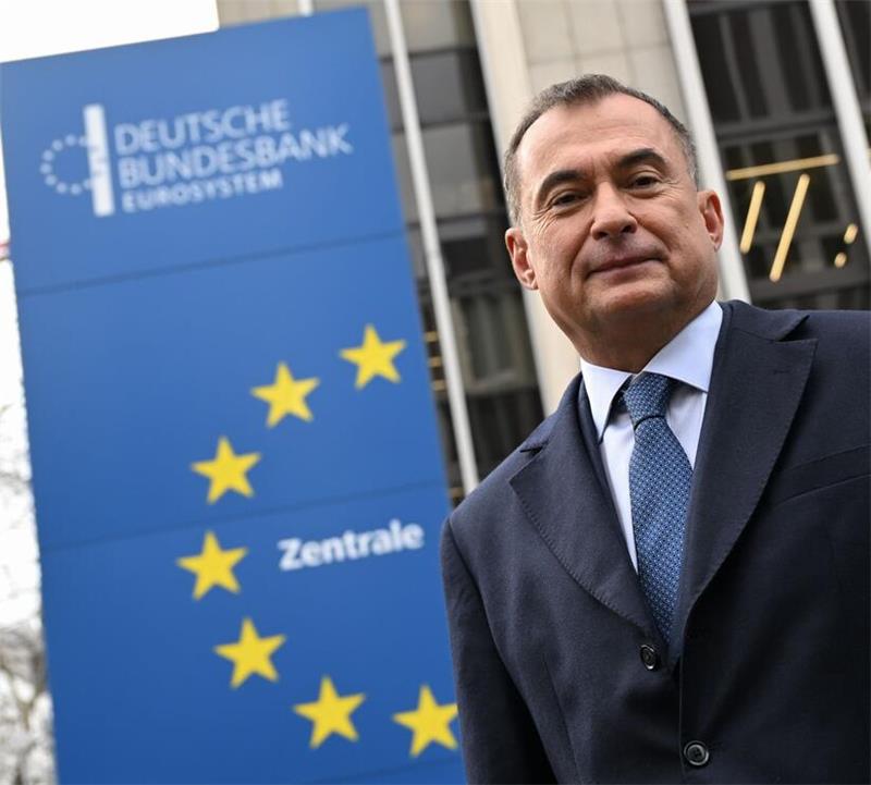 Mann in Anzug und Krawatte vor blauem Schild mit gelben Sternen und der Aufschrift 'DEUTSCHE BUNDESBANK EUROSYSTEM Zentrale'