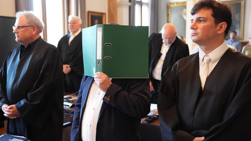 Prozess um teuren Schrott - Anwalt beklagt Unterstellungen Ein Angeklagter verdeckt im Hamburger Landgericht sein Gesicht mit einem Ordner. Zwei Lieferanten und ein Materialprüfer sollen den Hamburger Kupferhersteller Aurubis um Millionen betrogen haben.