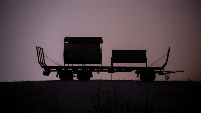 Ein Anhänger steht auf einer schneebedeckten Wiese bei Bitburg und wird von Straßenleuchten erhellt.