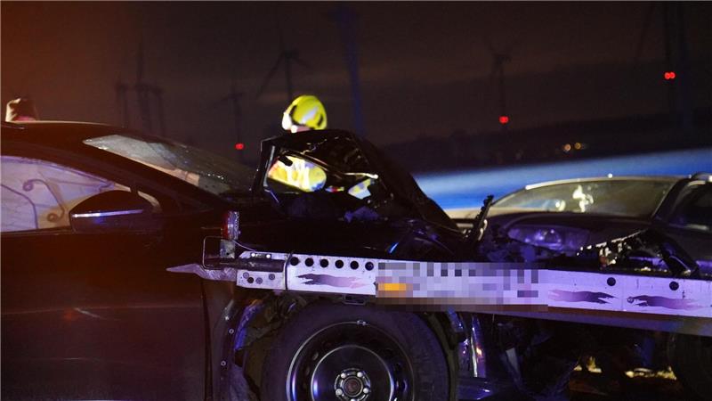 Ein Anhänger steckt in einem Motorraum eines schwarzen Unfallfahrzeugs.