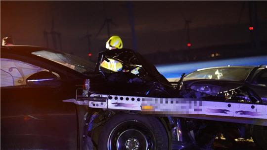 Ein Anhänger steckt in einem Motorraum eines schwarzen Unfallfahrzeugs.