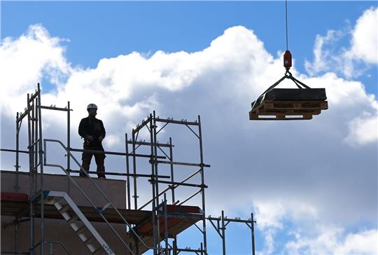 Ein Arbeiter dirigiert auf einer Baustelle einen Kran. Das Wirtschaftswachstum in Deutschland nimmt laut Bundesbank leicht zu.