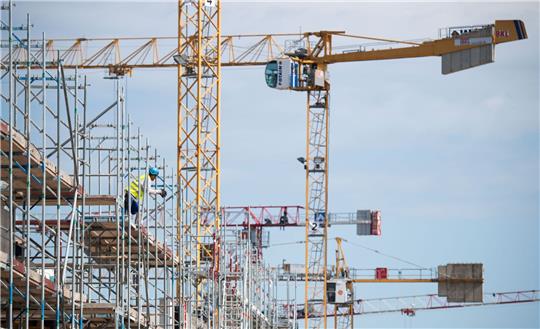 Ein Arbeiter steht auf einer Baustelle für Mehrfamilienhäuser auf einem Gerüst.
