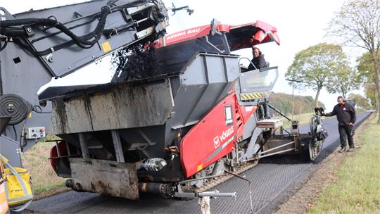 Ein Fertiger bringt Asphalt auf eine abgefräste Straße auf.