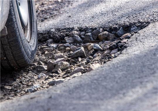 Ein Auto fährt durch ein Schlagloch: Immer mehr Unternehmen klagen über die teilweise marode Straßen in Deutschland.
