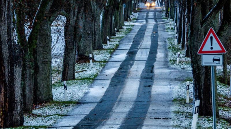 Ein Auto fährt durch eine leicht verschneite Allee. Leichter Schneefall und Temperaturen um die null Grad behindern den Verkehr in Norddeutschland.