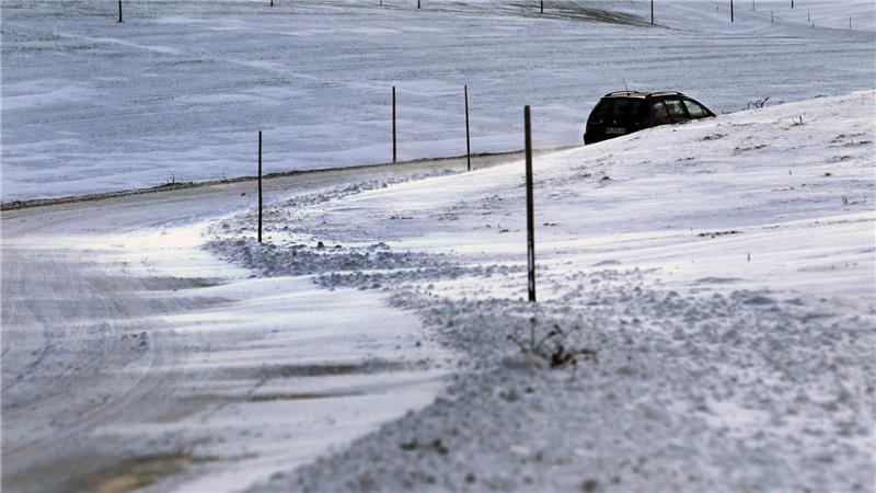 Ein Auto fährt über eine teilweise schneeverwehte Straße