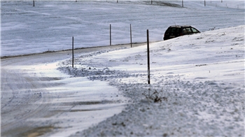 Ein Auto fährt über eine teilweise schneeverwehte Straße