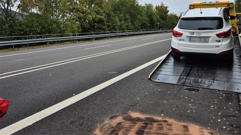 Weißes Auto mit Warnblinkanlage steht auf einer Rampe am Straßenrand einer mehrspurigen Straße mit Leitplanke und doppelter durchgezogener Linie