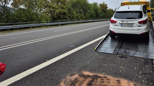 Weißes Auto mit Warnblinkanlage steht auf einer Rampe am Straßenrand einer mehrspurigen Straße mit Leitplanke und doppelter durchgezogener Linie