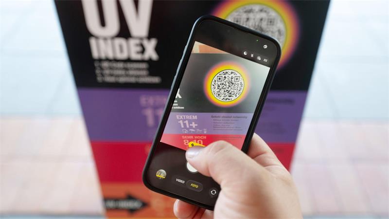 Ein Bademeister scannt am Vormittag eine UV-Index Anzeige mit einem Smartphone.