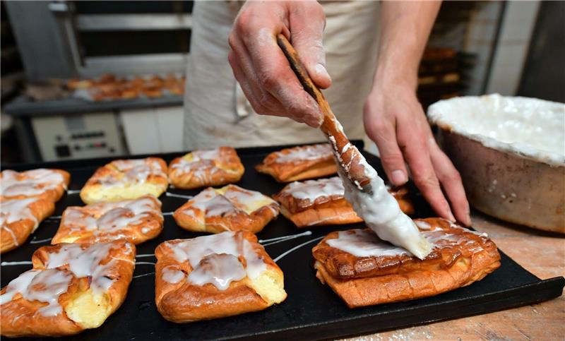 Ein Bäckermeister pinselt Zuckerguss auf süßes Gebäck in seiner Backstube.