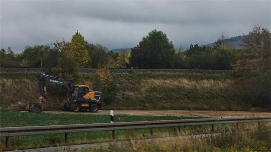Baggerarbeiten entlang einer Bundesstraße unter bewölktem Himmel. Im Hintergrund ein Bahngleis.