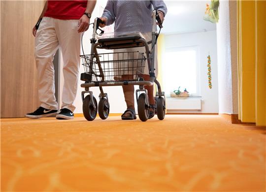Ein Betreuer geht in einem Pflegeheim mit einer Bewohnerin über den Flur. Foto: dpa