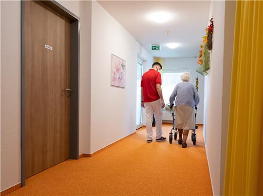 Ein Betreuer läuft in einem Altenheim mit einer Bewohnerin auf einem Flur. Symbolbild: Bernd Weißbrod picture alliance/dpa
