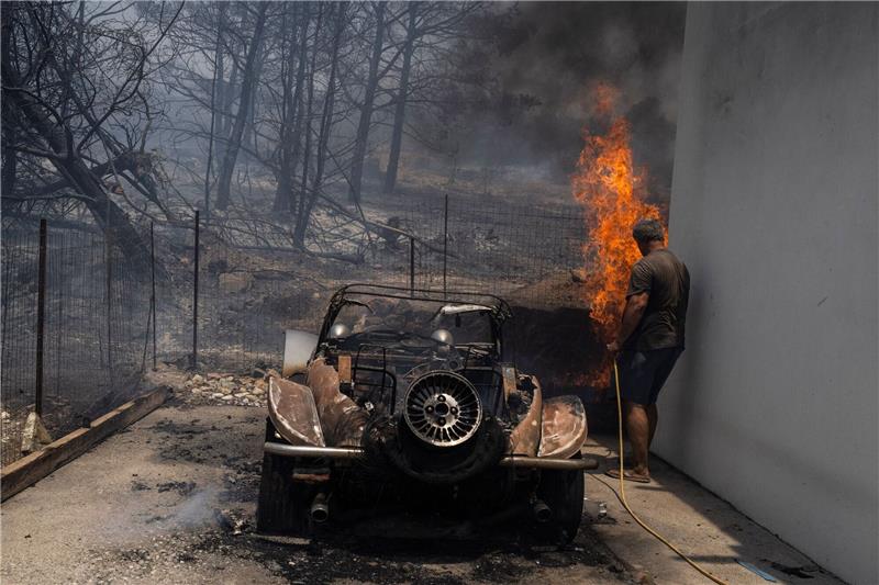 Brände auf Rhodos wüten weiter Ein Bewohner versucht, die Flammen im Hof eines Hauses zu löschen.