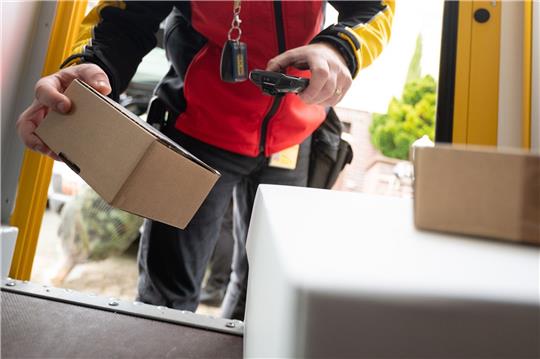 Ein DHL-Mitarbeiter scant ein Paket für die Zustellung.