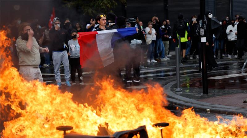 Ein Demonstrant der Protestbewegung „Bloquons Tout“ (Alles blockieren) zeigt eine französische Nationalflagge neben brennenden Mülltonnen.