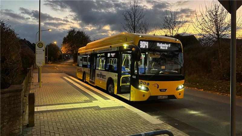 Ein Elektro-Stadtbus an einer Haltestelle in der Dämmerung
