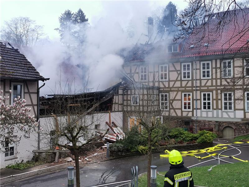 Ein Feuerwehrmann steht bei Löscharbeiten in der Nähe von den Klinik Gebäuden.