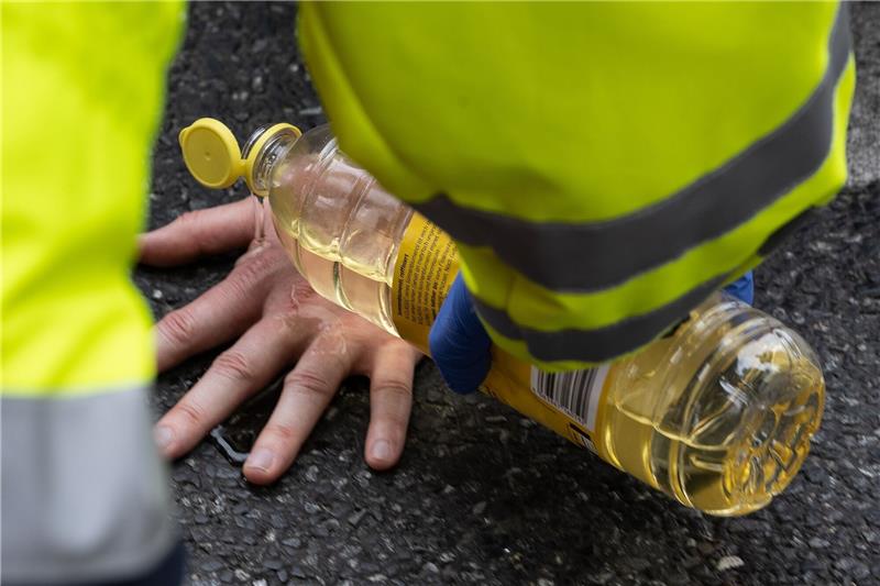 Ein Feuerwehrmann übergießt die Hand eines Aktivisten der Gruppe "Letzte Generation" mit Sonnenblumenöl.
