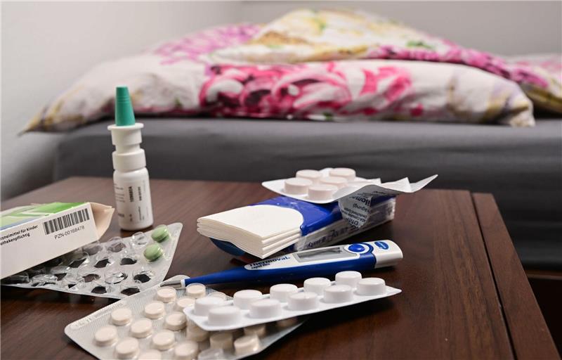 Krankheitswelle rollt: Arztpraxen und Kliniken am Limit Ein Fieberthermometer und Medikamente liegen auf einem Nachttisch.