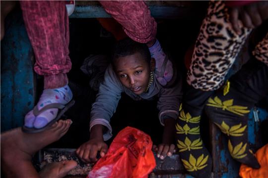 Ein Flüchtlingskind aus Eritrea versucht an der Küste zu Libyen, an Bord eines überfüllten Holzbootes hinaufzuklettern.