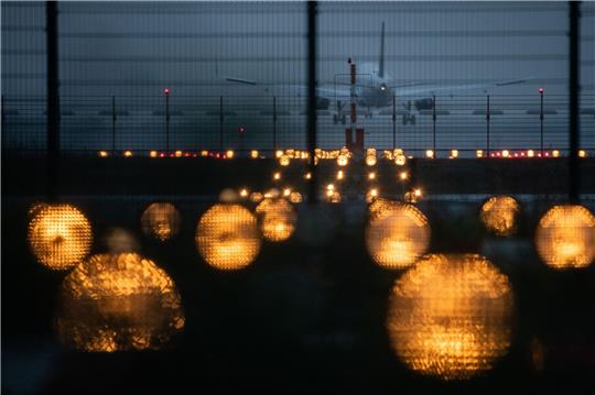 Ein Flugzeug landet hinter Signallichtern auf einem Flughafen.