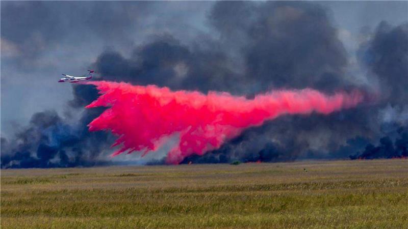 Ein Flugzeug wirft Feuerschutzmittel auf ein großes Waldfeuer.