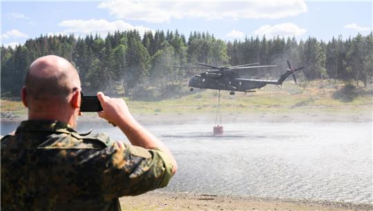 Ein Hubschrauber CH-53 der Bundeswehr entnimmt Wasser aus der Mandelholztalsperre zur Bekämpfung eines Waldbrandes bei Schierke. Foto:  Julian Stratenschulte/DPA