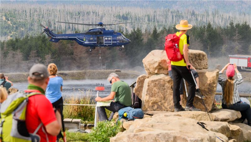 Brocken-Brand: Löschflugzeuge nach Harz-Einsatz zurück in Rom Ein Hubschrauber der Bundespolizei entnimmt Wasser aus einem See am Wurmberg, während zahlreiche Wanderer und Schaulustigen die Löscharbeiten beobachten. Hunderte Einsatzkräfte bekämpfen währenddessen den großen Waldbrand. Foto: Julian Stratenschulte, dpa