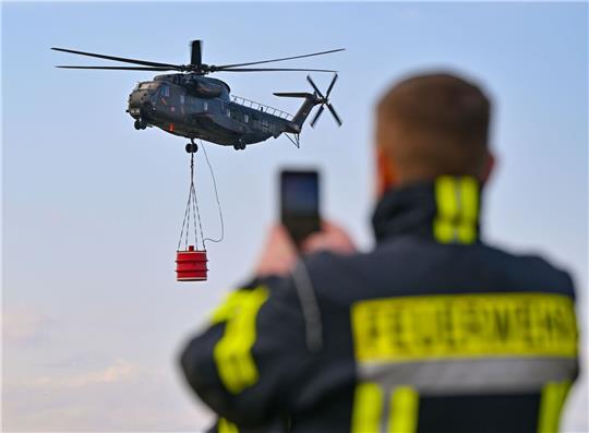 Ein Hubschrauber vom Typ Sikorsky CH-53 der Luftwaffe fliegt mit einem Wasserbehälter während einer Übung über den Flugplatz Müncheberg-Eggersdorf.