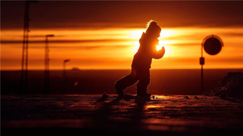 Ein Junge läuft bei Sonnenuntergang über eine Straße in Nuuk in Grönland.