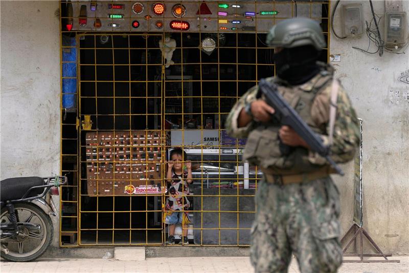 Vor Wahl: Weiterer Lokalpolitiker in Ecuador getötet Ein Junge schaut hinter den Gitterstäben eines geöffneten Elektronikgeschäfts hervor, während ein Soldat an einem von der Armee eingerichteten Sicherheitskontrollpunkt Wache steht.