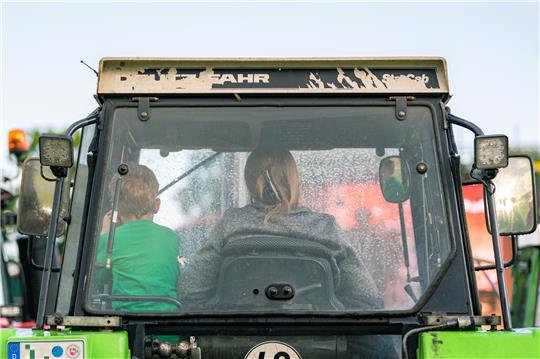 Ein Junge sitzt mit einer Frau in der Fahrerkabine eines Treckers. Bei einem Unfall mit einem Trecker wurde ein fünfjähriger Junge aus der Fahrerkabine des Traktors geschleudert und unter dem Fahrzeug eingeklemmt. Symbolfoto: picture alliance/dpa | Mohssen Assanimoghaddam